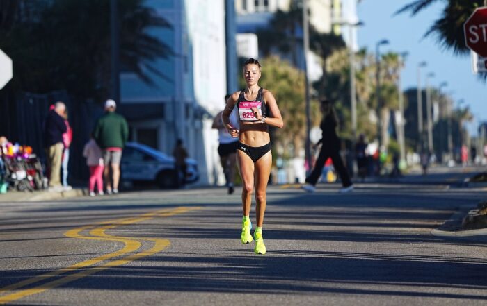 Female runner in a race on a sunny street wearing bright yellow shoes.